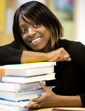 student smiling leaning on a stack of books.