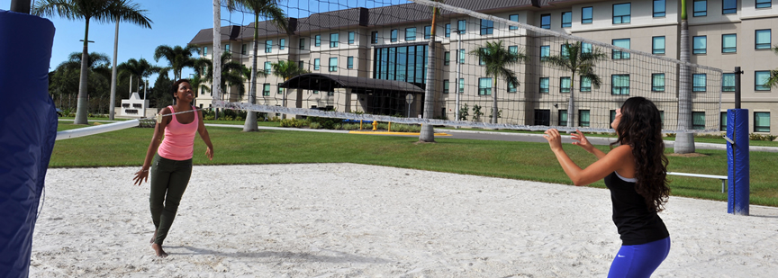 Two female students playing volleyball outside of the LightHouse Commons building. 