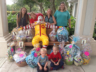 Kappa Delta Epsilon members with children, standing around a Ronald McDonald statue with gift baskets.