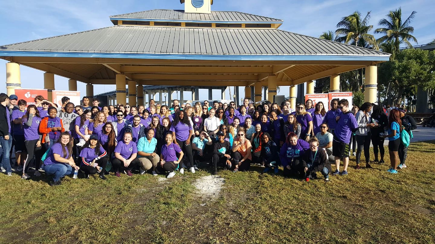 Large group of students in purple shirts posing in front of a gazebo.